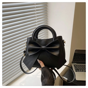 Detail of matte black handbag featuring a large bow and gold-tone metal hardware