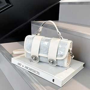 White cylinder crossbody bag with silver pattern and metal lock on stairs with a book