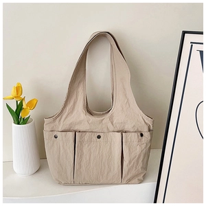 Detail showing beige nylon tote bag with three front pockets and metal buttons on white desk