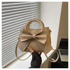 Detail of a cream faux leather tote bag featuring a large decorative bow and top handle