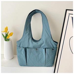 Detail of teal nylon tote bag featuring three front pockets with dark metal rivets