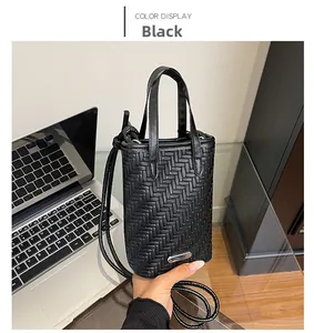 Close-up of black crossbody bag with woven texture and silver metal brand plate