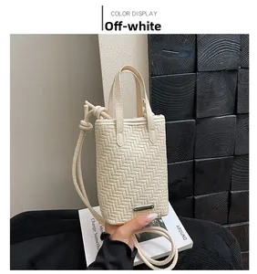 Detail of cream woven mini bag with adjustable shoulder strap and metal logo plaque