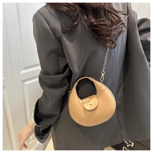 Détail d'un sac demi-lune beige avec chaîne dorée sur une tenue de blazer gris foncé