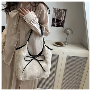 Detail of cream woven tote bag featuring black contrast leather bows and top handles