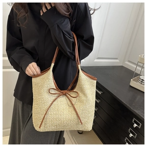 Close-up of beige straw tote bag featuring brown leather handles and a decorative bow