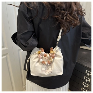 Close-up of white drawstring bucket bag with decorative marble bead handle shown in context