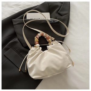 Detail of cream drawstring bucket bag with marble resin bead handle on black blazer