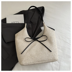 Détail d'un sac cabas tissé beige avec nœud noir et finitions en cuir sur tissu blanc
