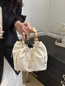 Cream drawstring handbag with vintage resin bead handle and bear emblem detail