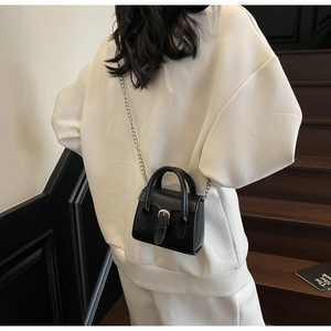 Nahaufnahme einer schwarzen Mini-Kettenumhängetasche mit Silberschnalle auf weißem Outfit