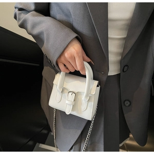 Detail einer weißen Leder-Minihandtasche mit silbernen Beschlägen und Metallkettenriemen