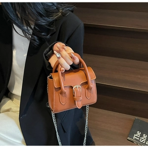 Detail of caramel leather mini handbag with vintage buckle and silver chain strap