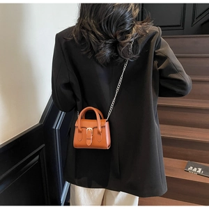 Mini sac à main marron avec bandoulière chaîne porté sur un blazer noir chic