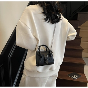 Detail of a black leather mini square bag with silver chain strap on a white hoodie