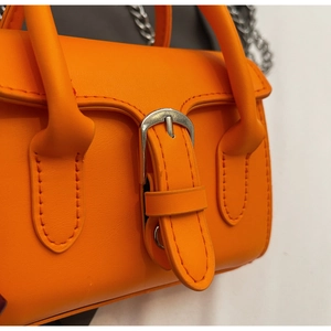 Detail of bright orange PU leather mini bag with silver buckle and metal chain strap