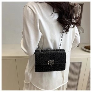 Detail of black faux crocodile texture bag with silver chain strap on model shoulder
