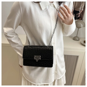 Close-up of black crocodile-embossed leather texture and dark chain strap on a chic bag