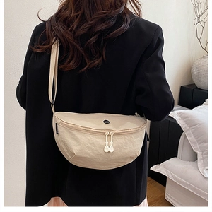 Model wearing a beige nylon crescent crossbody bag with a round OK logo and zipper detail