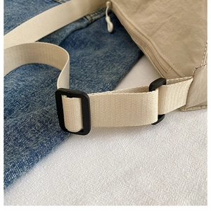 Detail of adjustable nylon shoulder strap and black plastic buckle on beige handbag