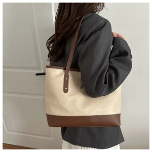 Detail of a large PU leather tote bag in beige and brown shown on a model's shoulder