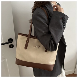 Close-up of a two-tone PU leather tote bag with a golden metal bow and brown shoulder straps