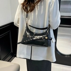 Glossy black underarm bag with gold hardware worn on a white suit for a retro chic look