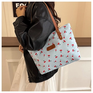 Detail of light blue tote bag featuring red cherry prints and brown leather handles