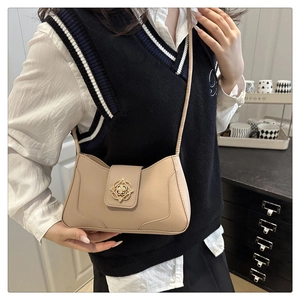 Detail of beige crossbody bag with a golden floral buckle worn by a female model