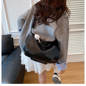 Détail d'un grand sac hobo en cuir souple noir avec un pompon blanc porté par un modèle