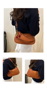 Detail view of brown pebbled leather crescent bag with chain strap and cherry charm