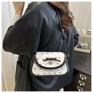 Close-up of bowknot detail and heart pendant on black and white patterned shoulder bag