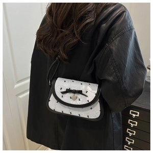 Close-up of white quilted bag with black bow detail and silver heart charm pendant