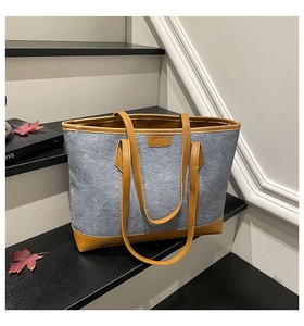 Detail view of large grey felt tote bag with brown leather trim on dark wood stairs