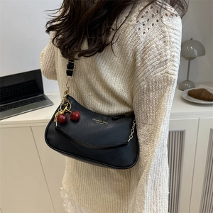 Modern black leather shoulder bag with cherry charm shown in a cozy home setting