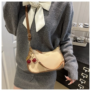 Detail of off-white lychee texture bag with cherry pendant and adjustable brown strap