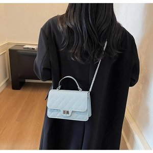 Detail showing the light blue quilted crossbody bag with a metal chain and turn-lock