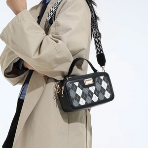 Stylish black and white quilted crossbody bag with geometric strap on a trench coat