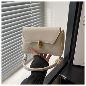 Dettaglio di una borsa a tracolla in pelle beige con chiusura in metallo dorato e cinturino a nodo