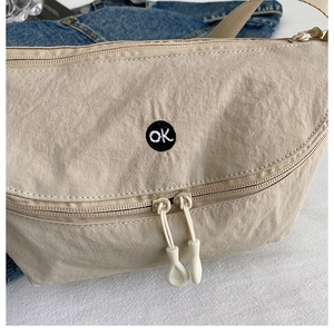 Detail of beige nylon crossbody bag with dual resin zippers and circular ok embroidery patch