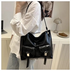 Close-up of a glossy black shoulder bag featuring dual front pockets and silver buckles