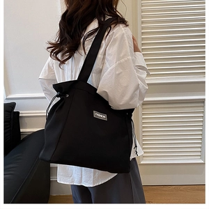 Detail of black canvas tote bag showing side drawstrings and Fashion brand tag on the side