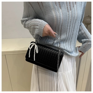 Detail of black woven handbag featuring pearl bow ornament and silver metal ring handle