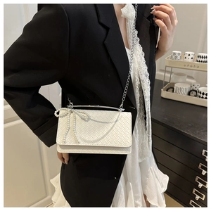 Detail of white woven texture bag with pearl bow decoration and thin metal chain strap