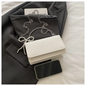 Detail of white woven square bag with silver metal handle and pearl bow charm accessory