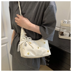 Detail of white half-moon bag featuring pearl bows, lace charms, and golden studs