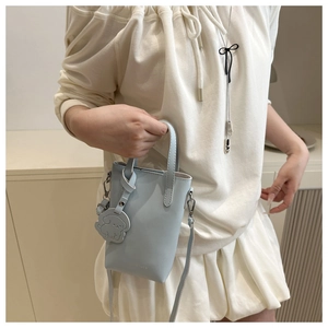 Detail of light blue mini bucket bag featuring a cute white dog charm and top handles