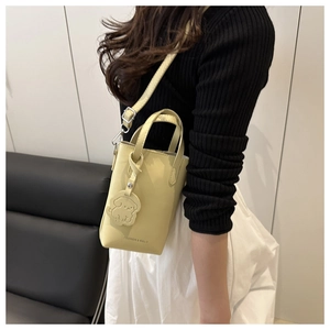 Détail du sac seau en cuir jaune clair avec breloque chiot et gravure fashion