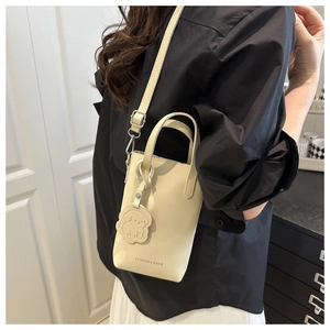 Detail of cream bucket bag with dog charm and adjustable strap shown on model