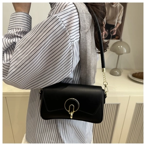 Close-up of a black leather underarm bag with a golden ring buckle and chain strap detail